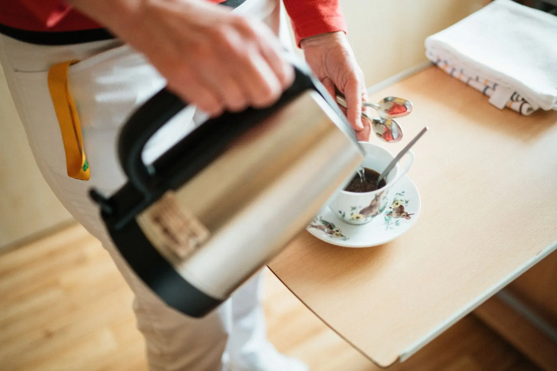 A caregiver pouring a hot drink into a cup on a tray table