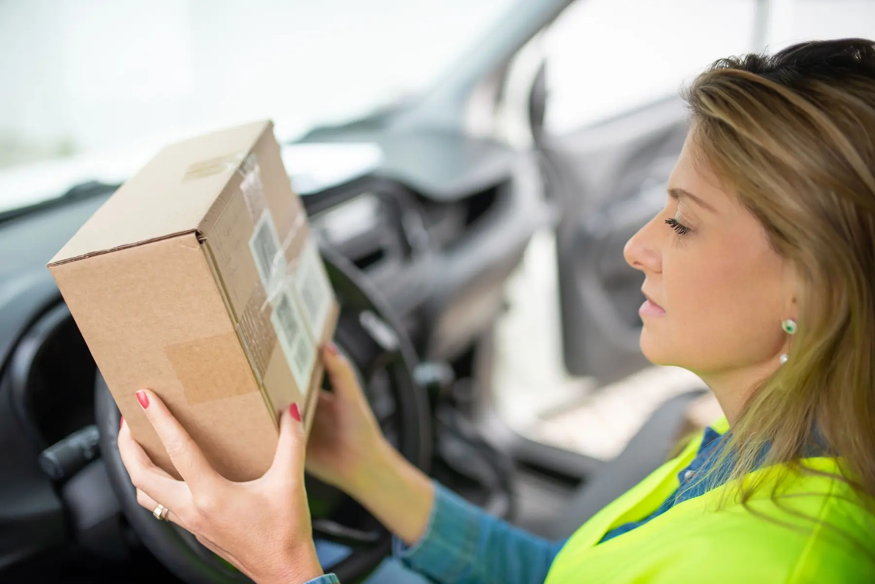 A courier in a high-visibility vest checking a parcel in the driver seat