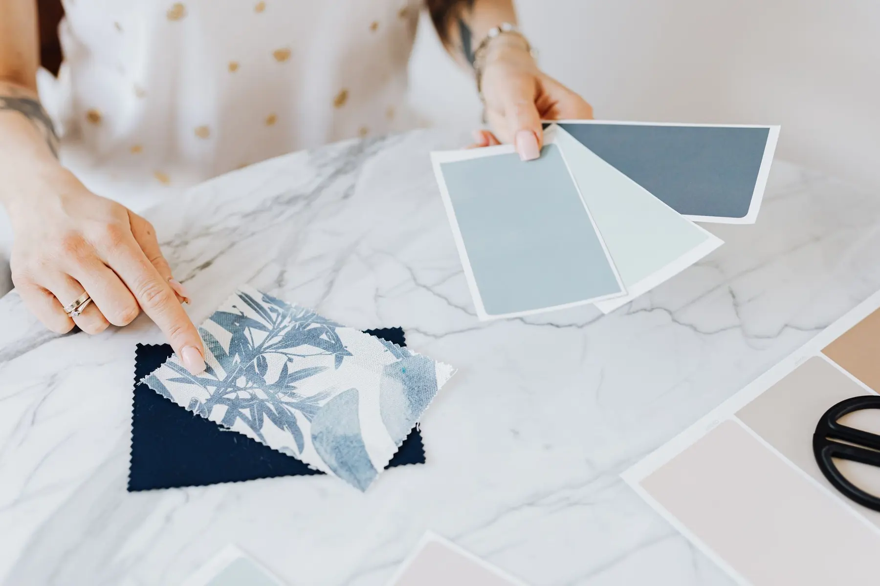 An interior designer's hands with fabric and paint swatches on a marble table