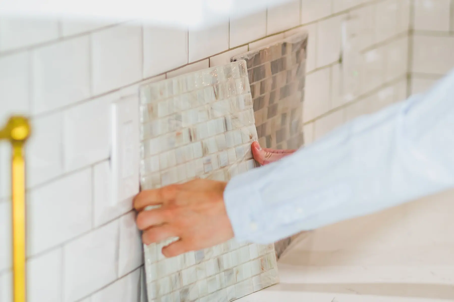 A hand setting a sheet of tile on a kitchen backsplash